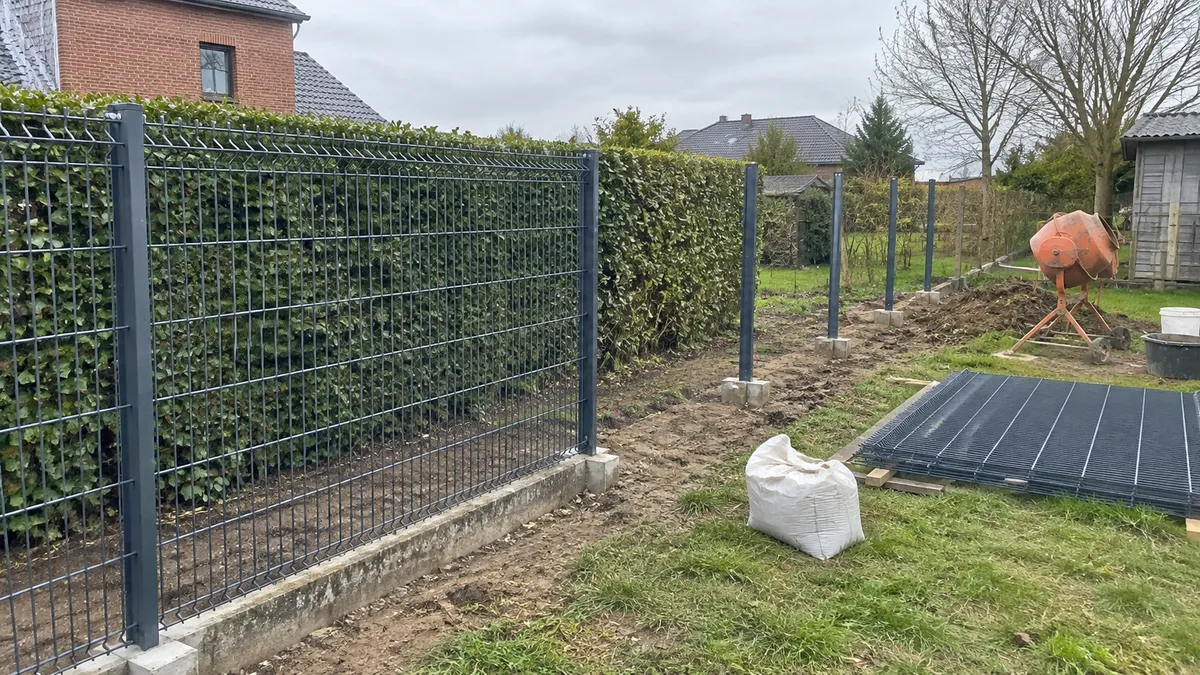 Pose de panneaux rigides sur poteaux scellés le long d'un jardin